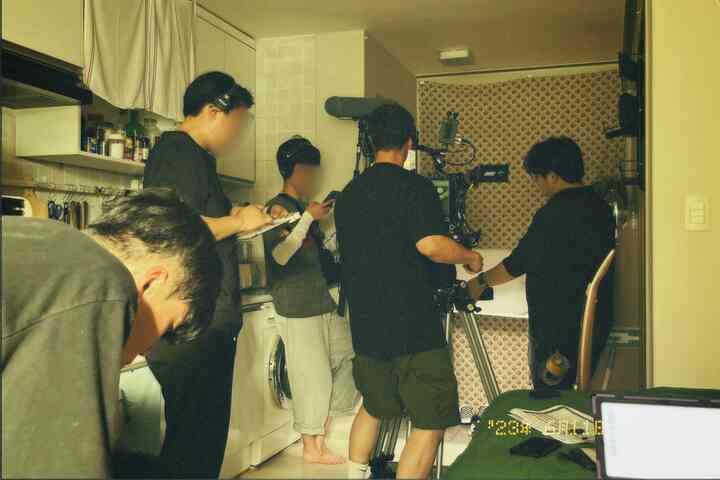 白を基調としたコンパクトなキッチン空間に撮影機材とスタッフが配置された多目的作業スペース