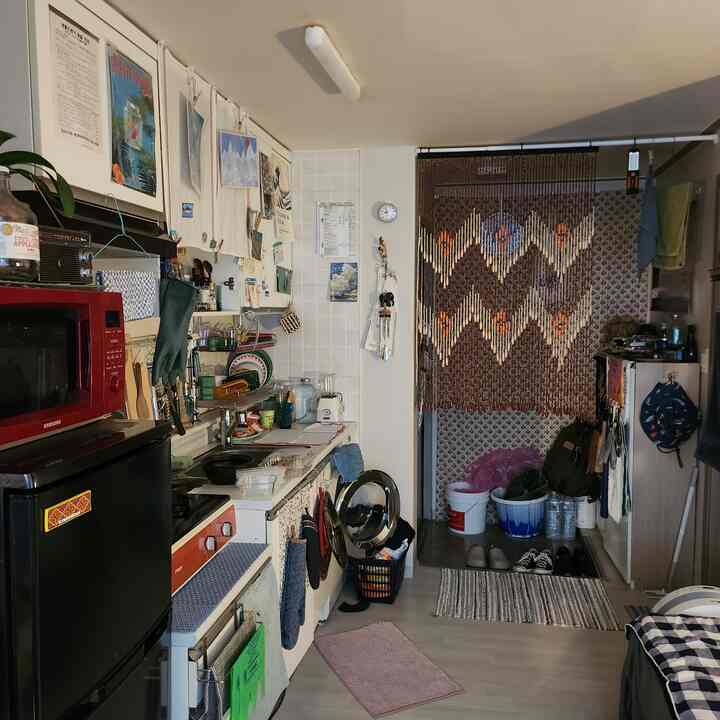 白と茶色の色調の狭いワンルームキッチン、ベランダ入口にビーズのカーテンと多様な調理器具が配置された雰囲気のあるインテリア