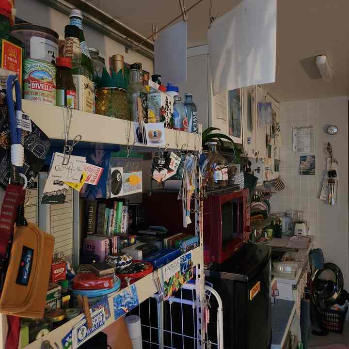 白と黒のトーンが混ざる狭いキッチン、びっしりと配置された棚と多彩な小物で個性豊かに演出された空間