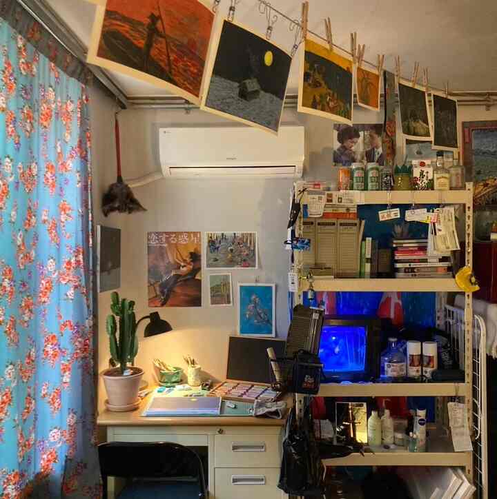 花柄のカーテンと多目的デスクがあるワンルームのホームオフィス、天井に掛けられたポスターとヴィンテージアイテムが雰囲気ある空間を演出