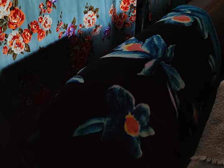 ヴィンテージ風の花柄が目立つブルーグレーのカーテンと濃い色の花柄ブランケットが置かれた落ち着いた空間