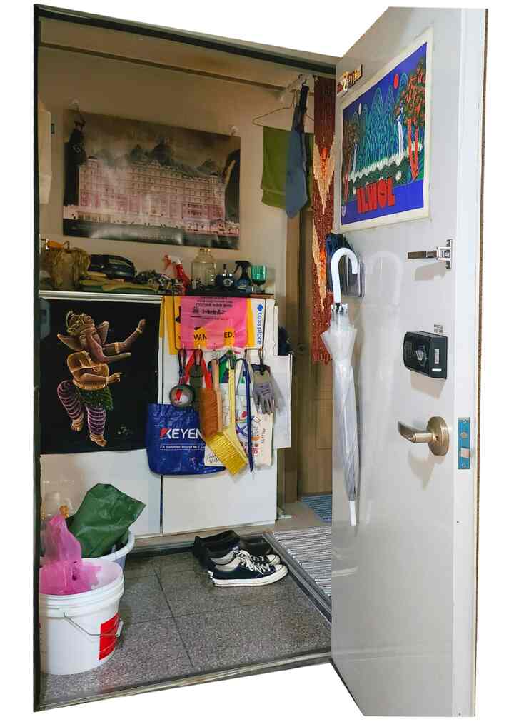 白を基調とした玄関スペースに靴箱と掃除用具が整頓され、壁には複数のポスターが飾られた印象的な入口