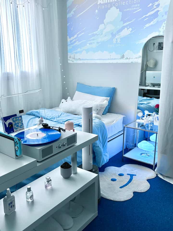 明るい青と白のトーンのワンルーム寝室、ベッドと青いターンテーブル、鏡が配置された居心地の良い空間