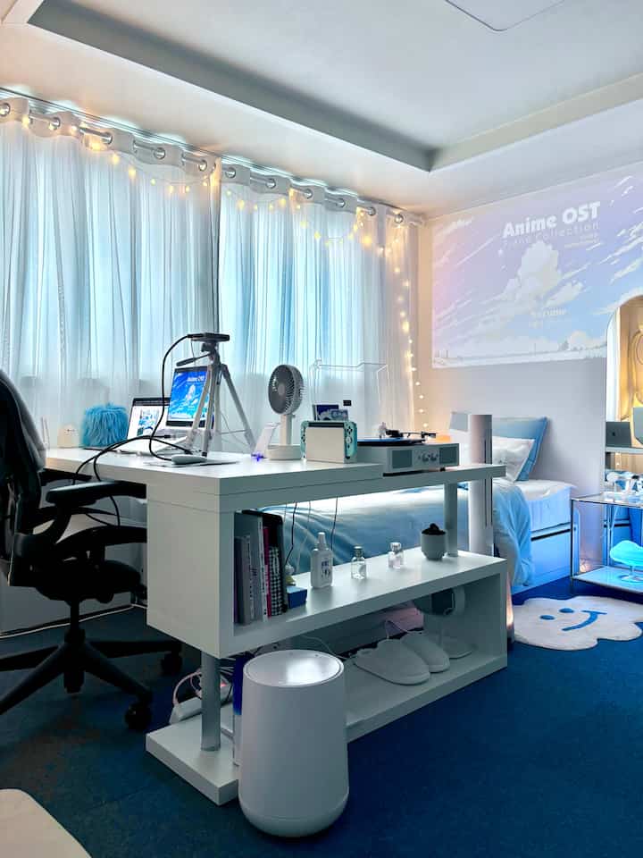 ホワイトとブルーのトーンが広がる寝室兼ホームオフィス、広いデスクとベッド、カーテンが調和する雰囲気のあるインテリア