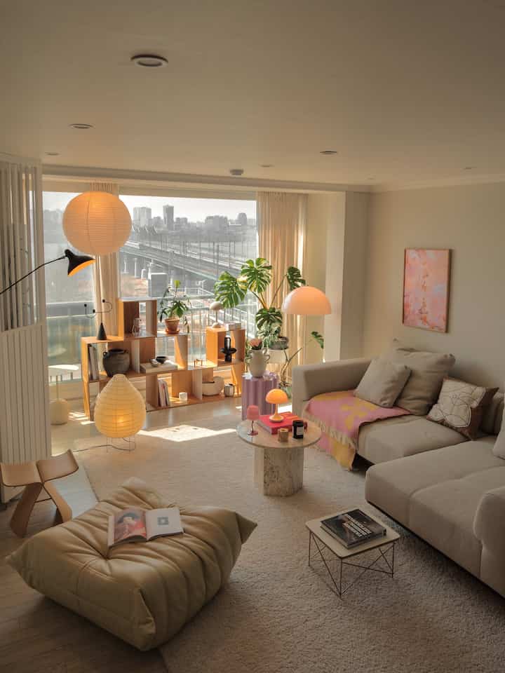 柔らかなベージュとホワイトの色調のリビング、自然光が差し込む窓辺に植物とソファが配置された雰囲気のあるナチュラルモダンなインテリア