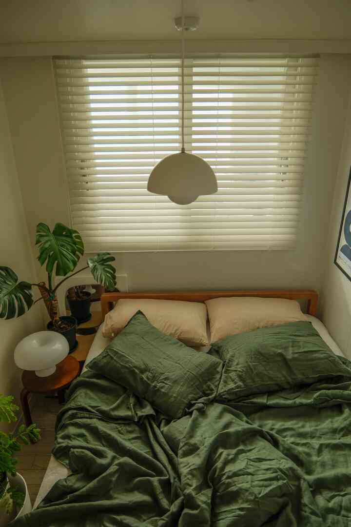 ベージュとダークカーキグリーンの寝室、木目調ベッドとペンダントライト、植物が配置された温かみのあるヴィンテージなインテリア