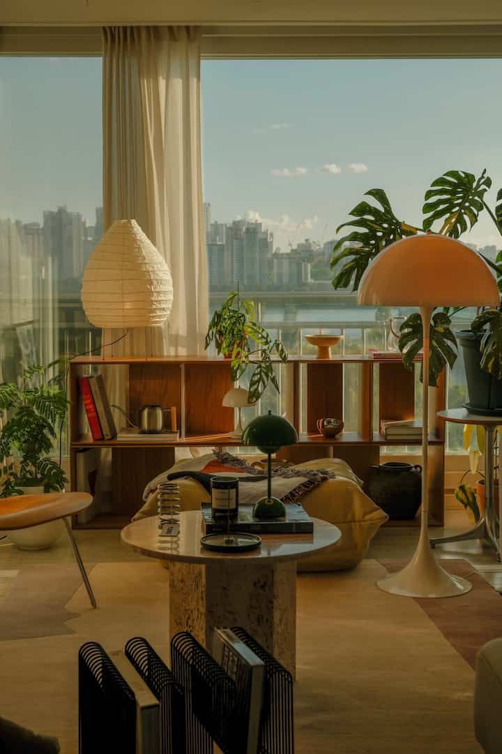 温かみのあるナチュラルな色調のリビング、広い窓と木製家具、多様な植物が配置された雰囲気のある空間