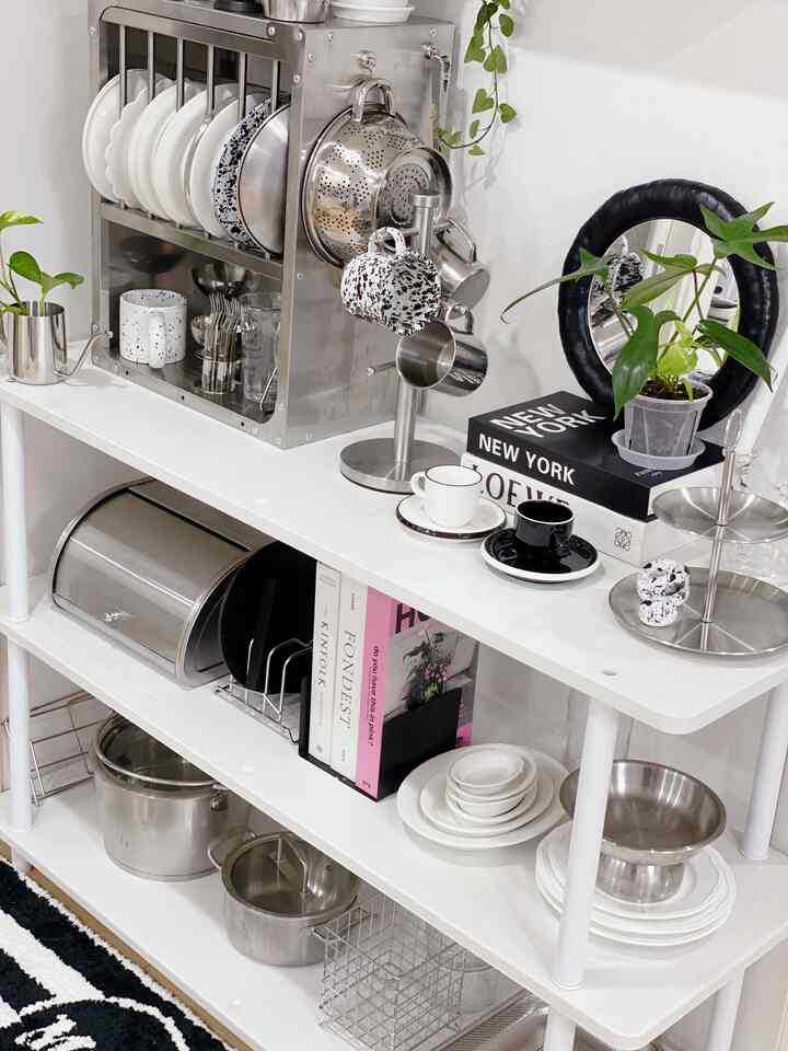 ホワイトトーンのキッチンシェルフ、ステンレス製の食器やボウル、植物が配置されたモダンで清潔感のあるキッチンスペース