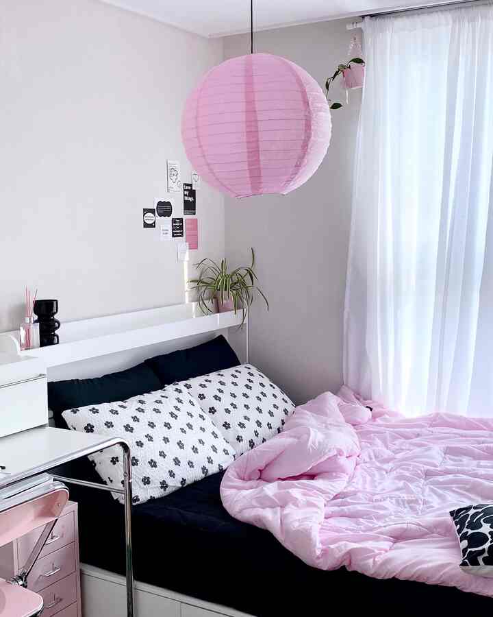 明るいピンクと黒、白のトーンの寝室、ピンクのペンダントライトと居心地の良い寝具が印象的な空間