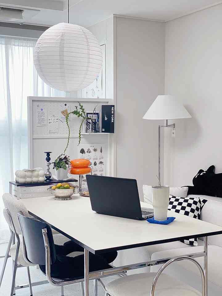 白を基調としたリビング兼ホームオフィス、中央にダイニングテーブルと椅子が配置され、モダンな照明とオブジェがある印象的な空間