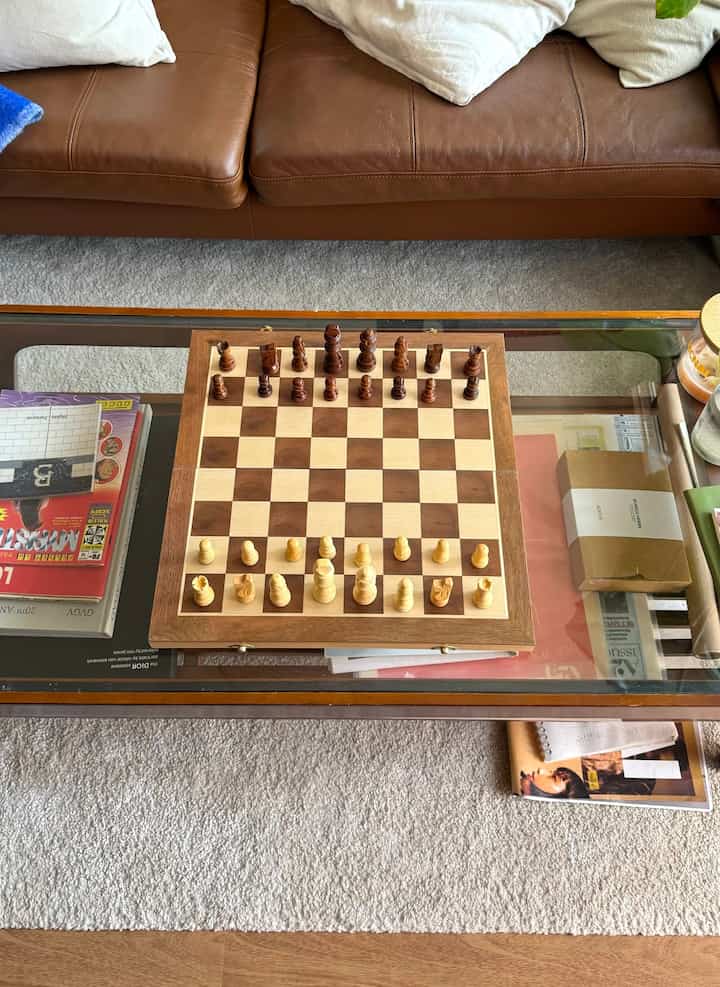 ブラウンレザーソファと透明なガラスのローテーブルがある居心地の良いリビング、中央にチェスセットと本が配置された雰囲気のあるインテリア