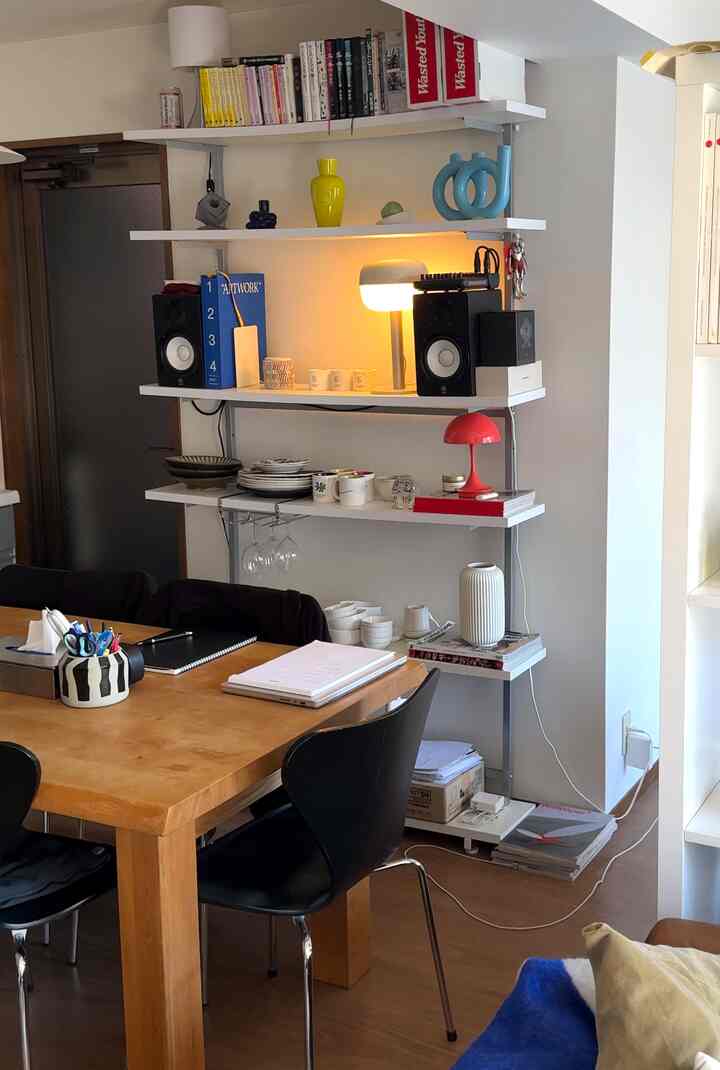 温かみのある木目調と黒い椅子が配されたダイニング、壁に配置された棚と照明が調和するシンプルモダンなインテリア