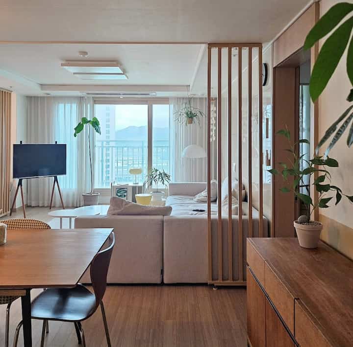 明るいホワイトと木目調のリビングとダイニング、木製スラットの間仕切りと植物が自然でモダンな雰囲気を演出