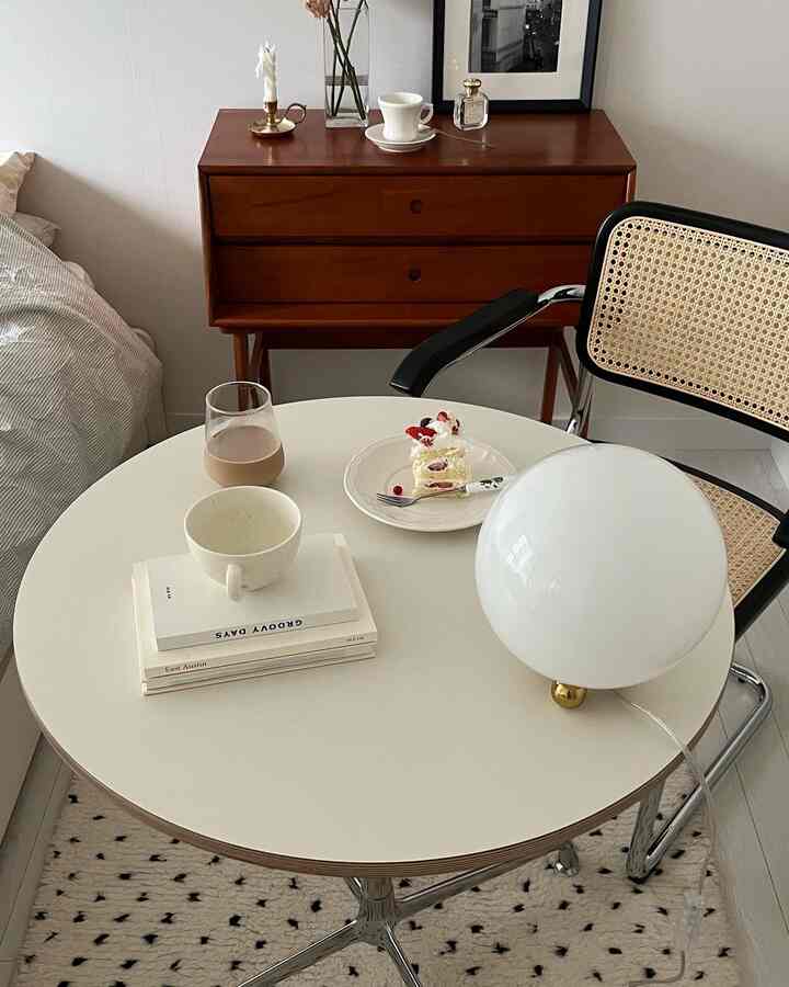 白と茶色の調和が取れたミニマルな一人暮らしの部屋、丸テーブルと椅子、テーブルランプが配置された空間