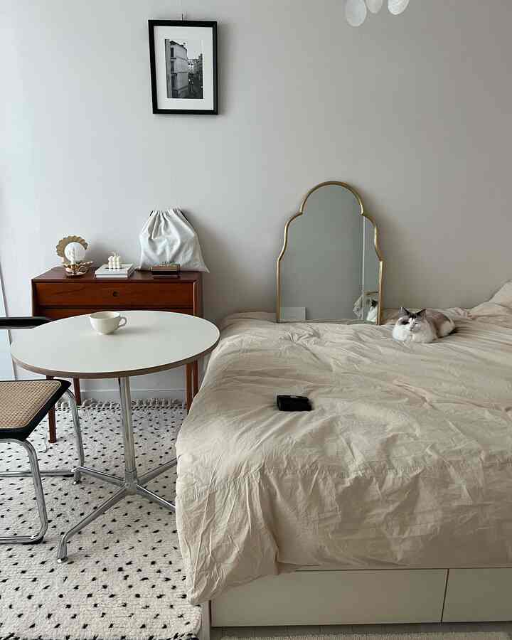 ベージュの色調の寝室、ベッドと丸いテーブル、猫がいるシンプルでナチュラルな雰囲気のインテリア