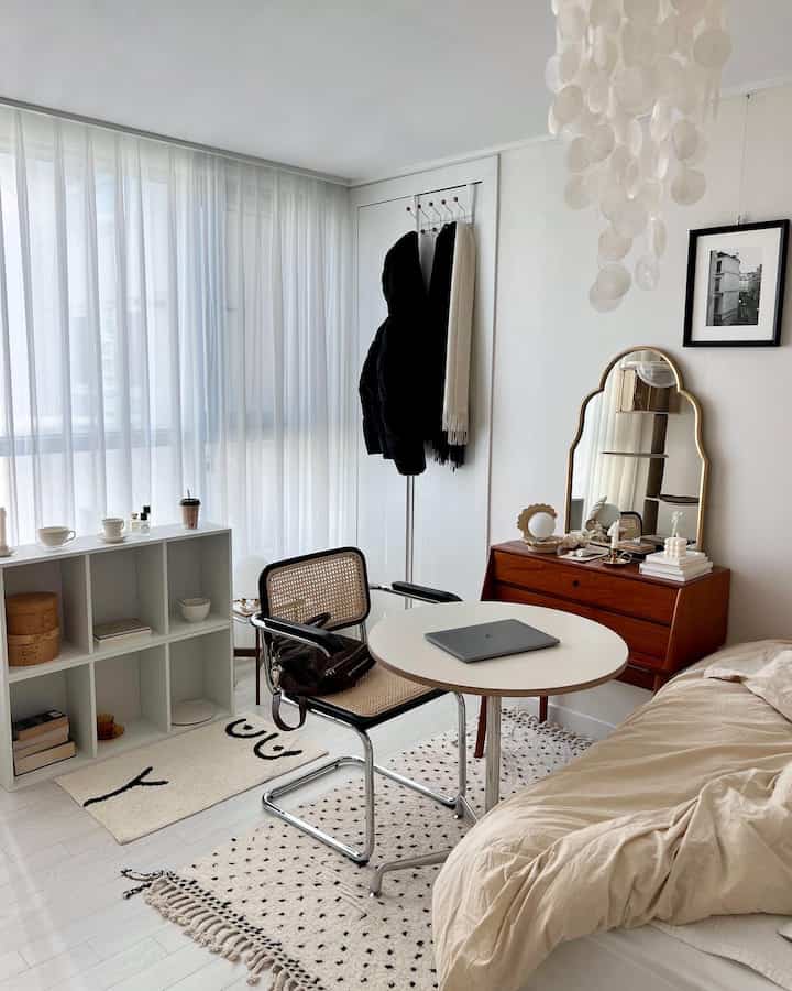 ナチュラルな色調の居心地良い寝室、木製チェストと丸テーブル、ラタンチェアが置かれたシンプルな空間