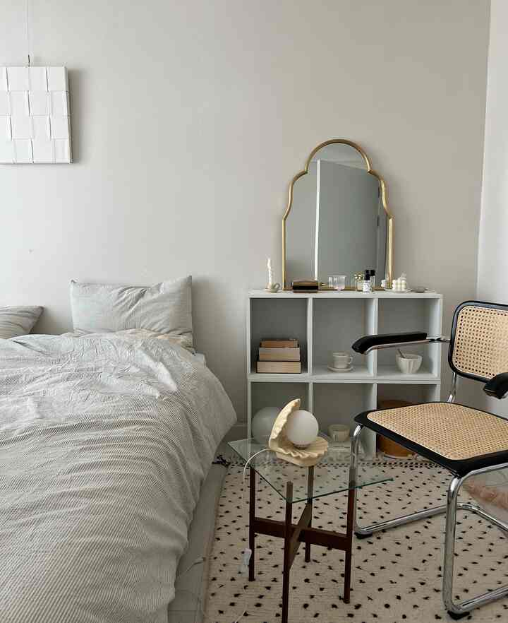 白と茶色の色調が調和した寝室、ベッドと金色の鏡、ガラスのサイドテーブルが配置された落ち着いた空間