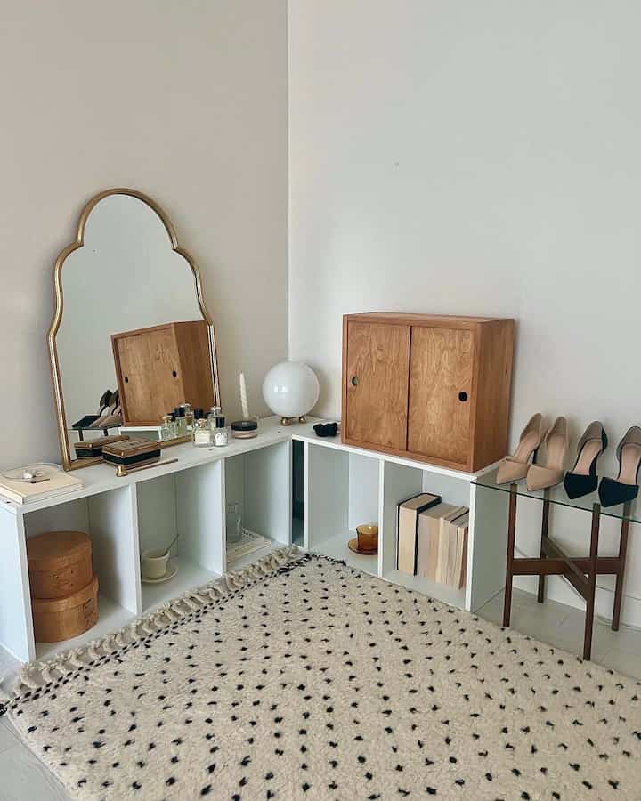 白い壁とナチュラルな木製収納家具が配されたコーナー空間、ドット柄ラグとガラスのサイドテーブルが調和するシンプルモダンなインテリア