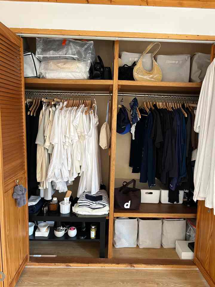 木目調のビルトインクローゼットが中心の収納空間、整頓された白と濃色の衣類と収納ボックスが配置された実用的で自然な雰囲気のインテリア