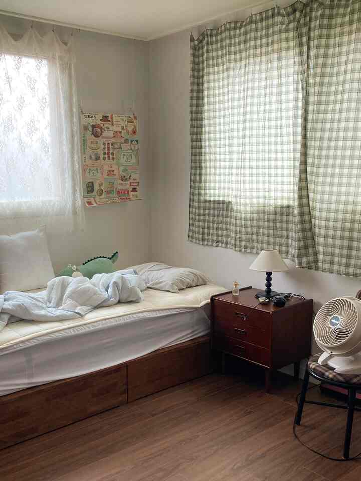 ウッドトーンとホワイトの寝室、木製ベッドフレームとナイトテーブル、カーテンとポスターが配置された居心地の良いインテリア