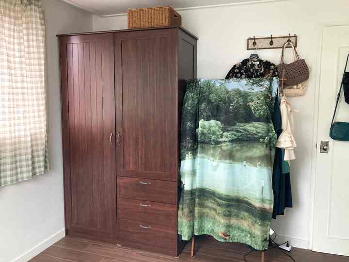 茶色の木製ワードローブとベージュカーテンがある狭いクローゼット、コートハンガーに服やバッグが掛けられた雰囲気のある空間