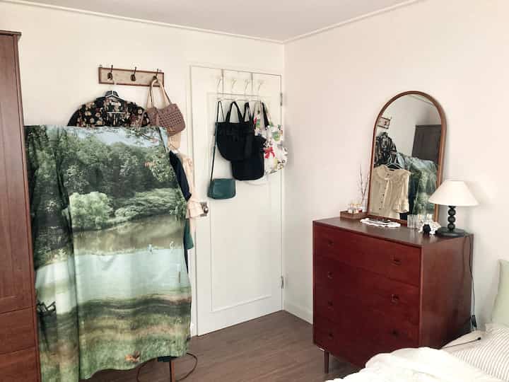 白い壁と茶色の家具が配置された寝室、ドレッサーの上に鏡とテーブルランプが置かれた雰囲気のある空間