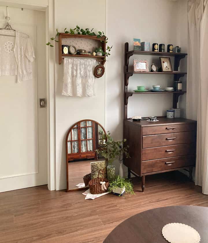 ナチュラルな木目調の床とヴィンテージスタイルの収納棚、鏡が配置された落ち着いた雰囲気のある空間