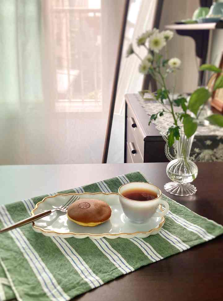 白と透明なガラス素材が調和したおうちカフェの空間、ヴィンテージのティーカップと皿が配置された雰囲気あるテーブルセッティング