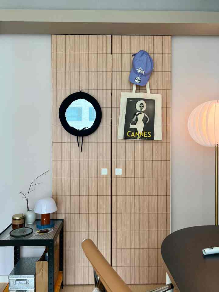 ナチュラルな色調のリビングルーム、中央に木目調のクローゼットがあり、丸い鏡とアクセサリーが配置された雰囲気のあるインテリア