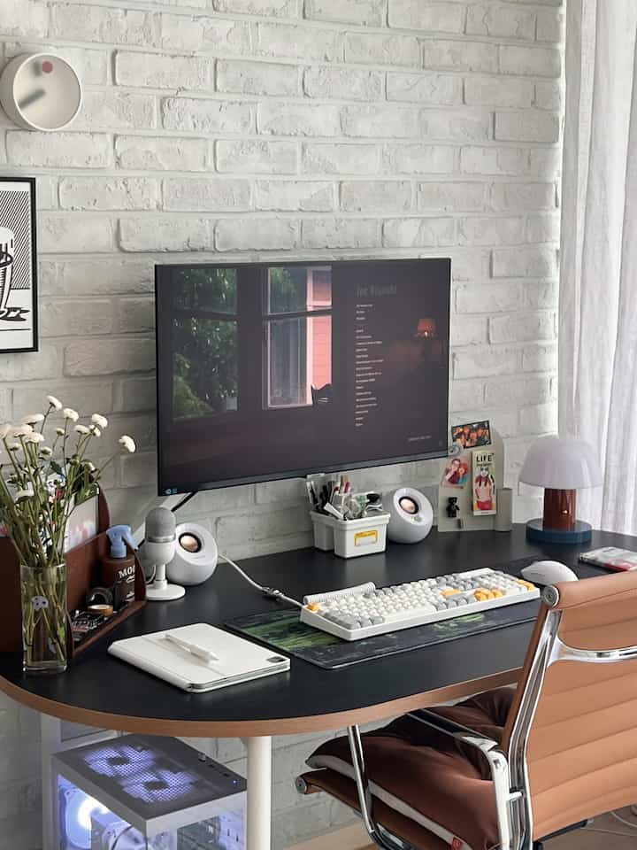 白いレンガの壁と黒い机があるホームオフィス空間、コンピュータモニターとオフィスチェアが配置された整然とした作業環境