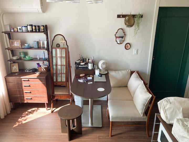 木目調の床と家具、白い壁、緑のドアがある狭い部屋のモダンなホームカフェ兼ワークスペース