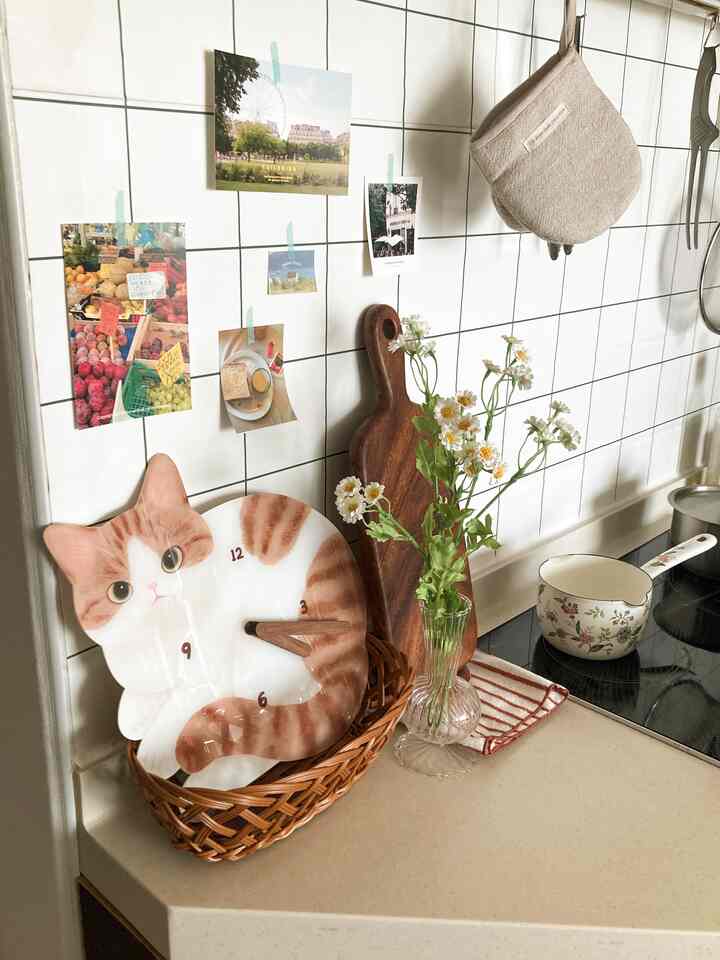 ナチュラルカラーのキッチン、猫型の壁掛け時計と造花が配置された雰囲気のあるインテリア