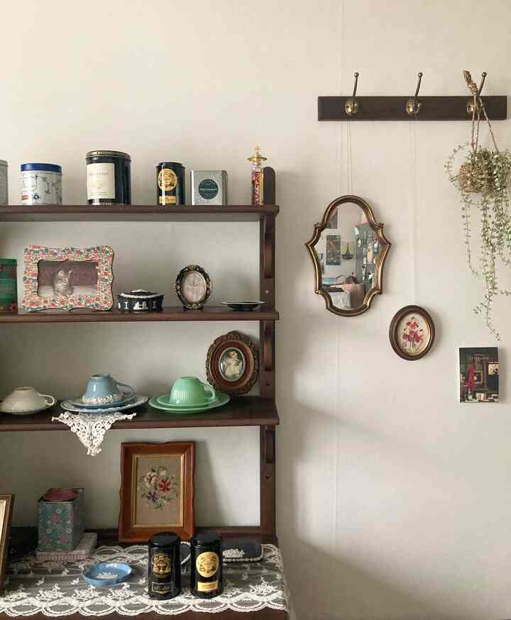 ナチュラルな木目調の壁面に、複数の額縁やミラー、ハンギングプラントが配置された温かみのあるインテリア