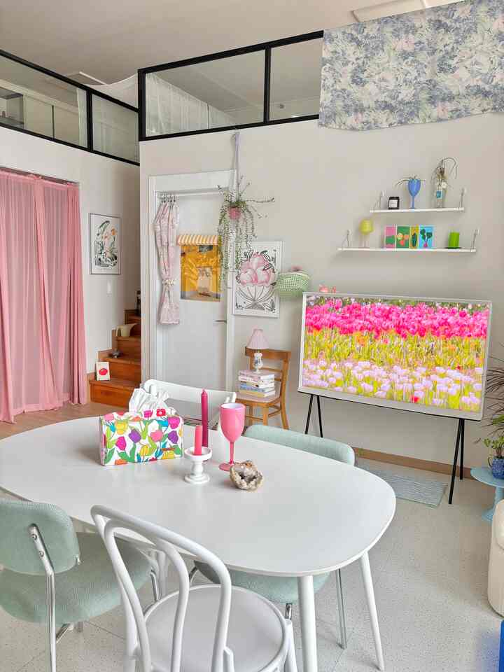 白とピンクのトーンでまとめられたコンパクトなリビング兼ダイニング、中央に白いダイニングテーブルと椅子が配置された雰囲気のある空間