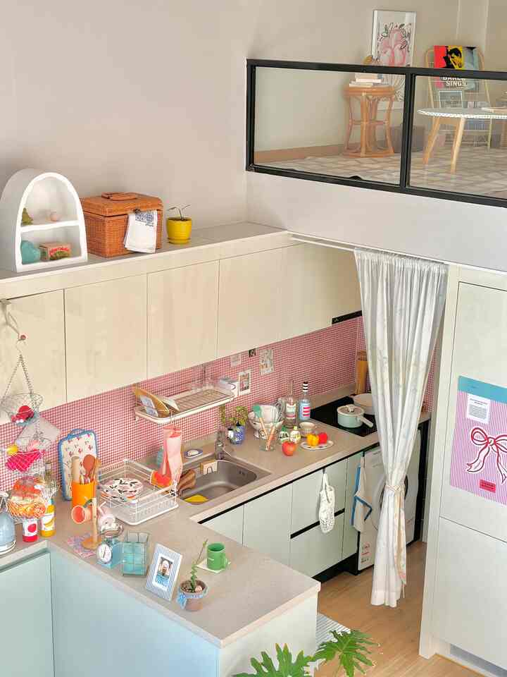 明るい白とナチュラルトーンの複層構造キッチン、赤のギンガムチェックの壁面と整理されたキッチン用品が配置された雰囲気のある空間