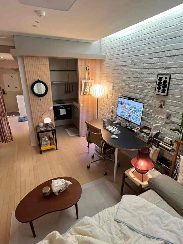 明るい白いレンガ壁とブラウンの木目調家具が配置されたホームオフィス兼リビングの雰囲気ある空間