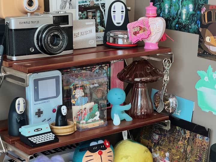 温かみのある木目調の棚に千と千尋のキャラクター、レトロなゲーム機、ヴィンテージカメラが並ぶ雰囲気のあるインテリア