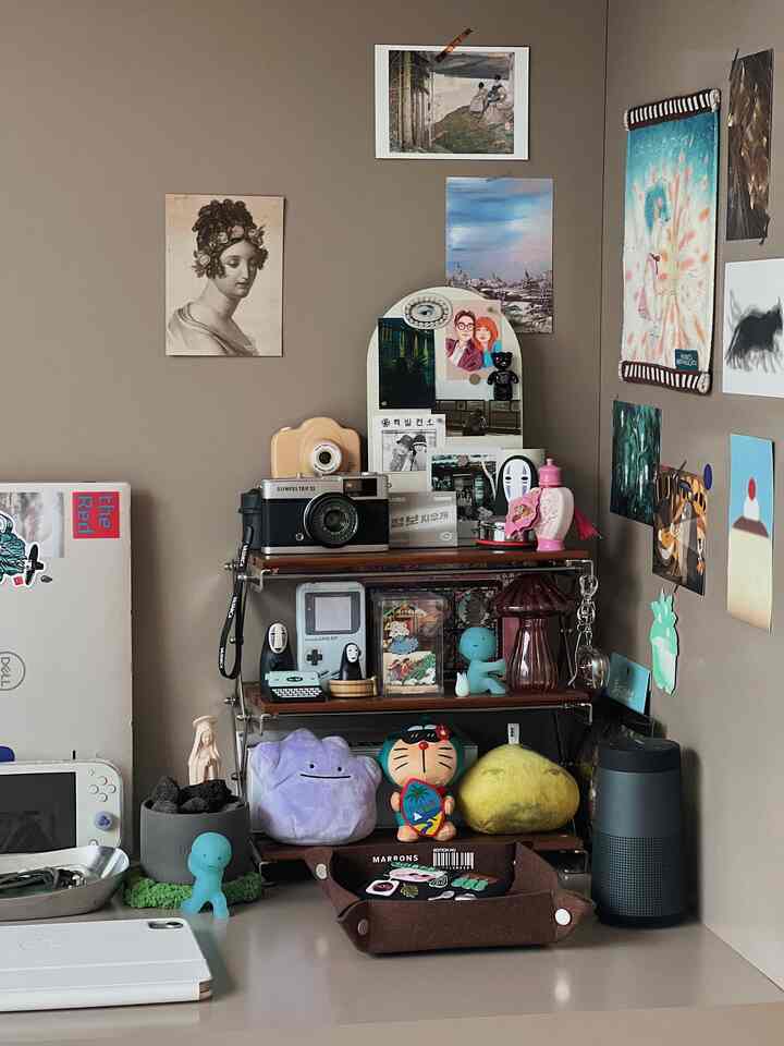 ブラウン調の壁と棚があるコンパクトなホームオフィス空間、多様なゲーム機とオブジェが配置された居心地の良い作業スペース
