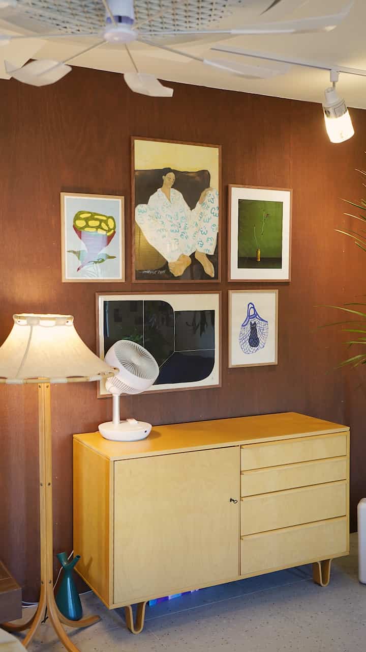 木目調の壁と淡いベージュ色のサイドボード、多様な額縁ポスターが飾られたシンプルなリビング空間