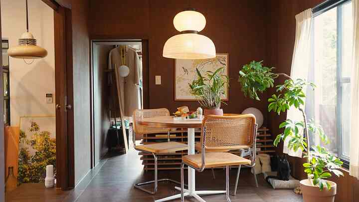 木目調の壁と床のナチュラルなダイニングルーム、丸テーブルと椅子、植物、白いカーテンが配された雰囲気のある空間