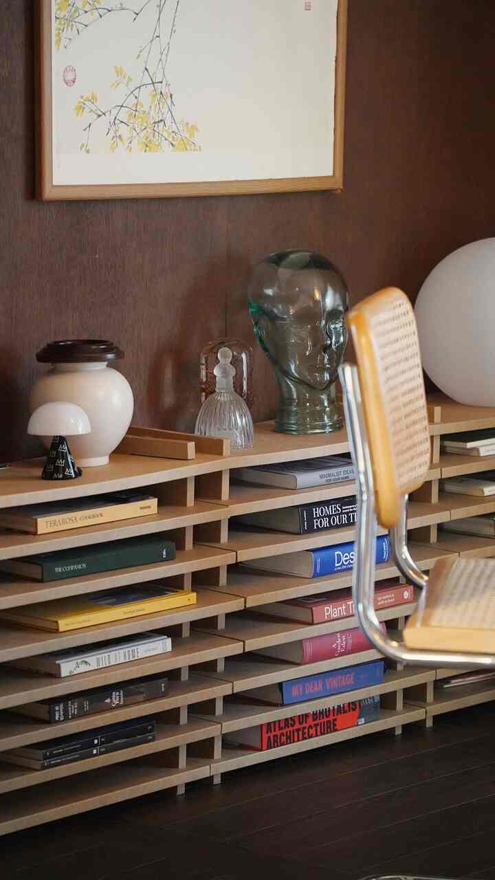 ナチュラルなウッドトーンのリビング、紙家具の本棚にアートブックやインテリア小物が整然と配置された落ち着いた雰囲気のインテリア