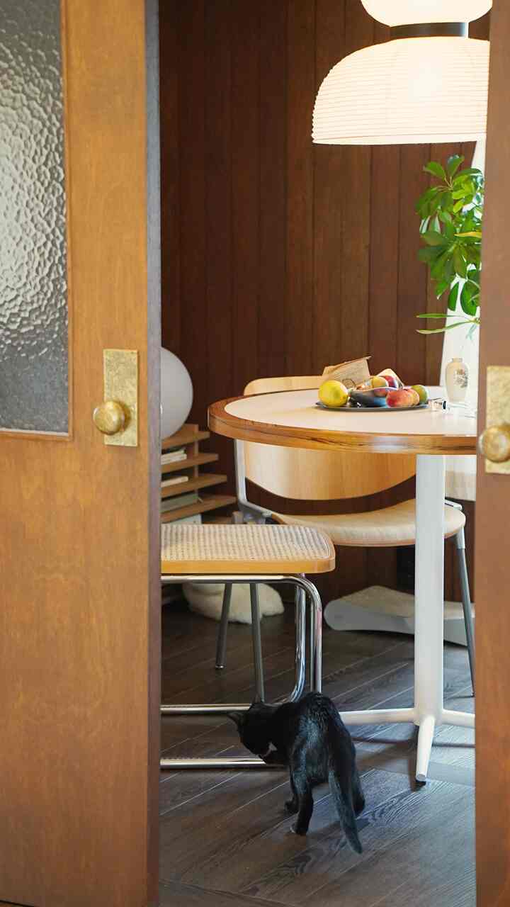 温かみのある木目調のキッチン、丸いダイニングテーブルと椅子の周りに猫とキャットタワーが配置された雰囲気のあるインテリア