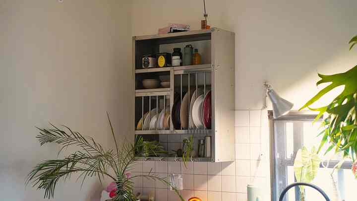 白いタイル壁とステンレス製収納があるキッチン、食器と植物が配置された明るく整った空間