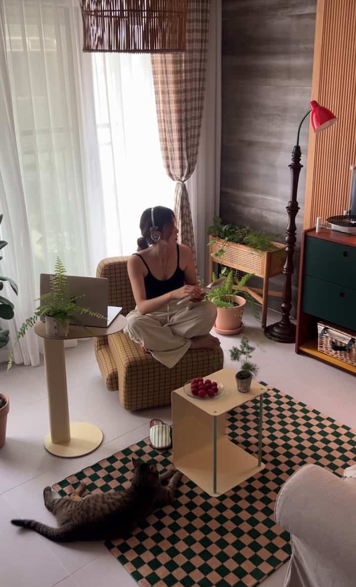 ナチュラルな色調のリビング、黄色のチェック柄ソファとチェック柄ラグが配置されており、ペットの猫がくつろいでいるシンプルなインテリア