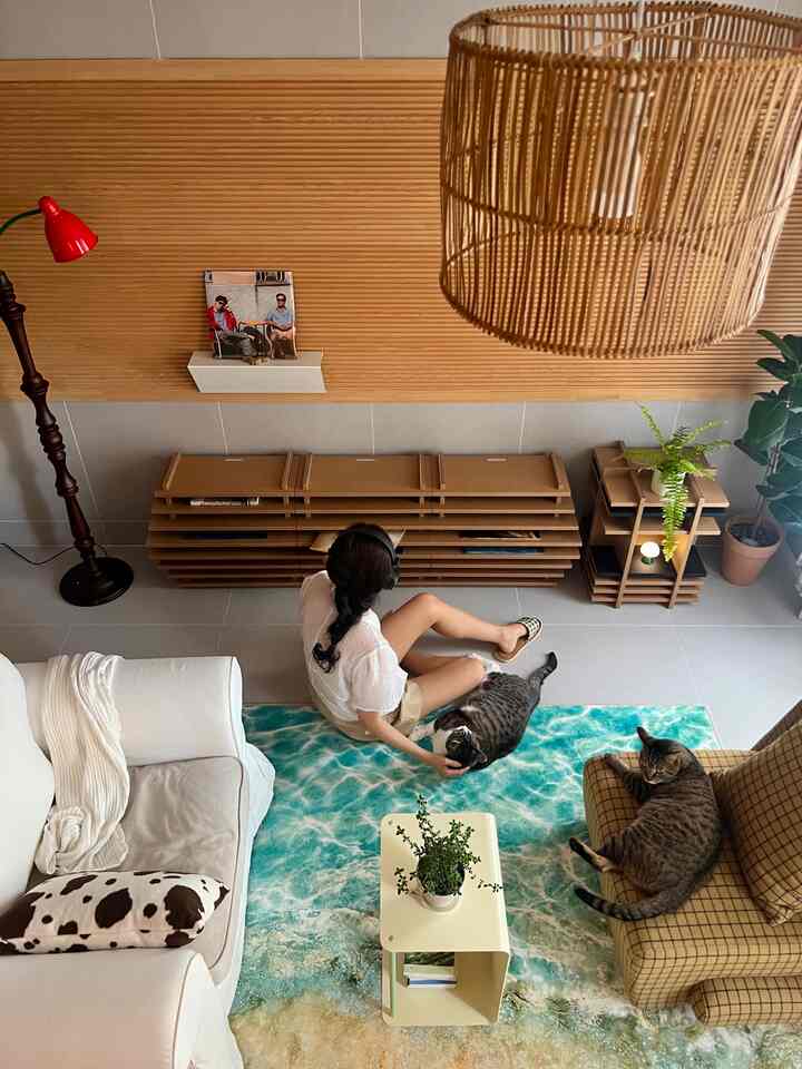 木目調の壁と照明がある明るく居心地の良いリビング、白いソファとチェック柄のアームチェア、海の模様のラグ、そして2匹の猫がいる空間