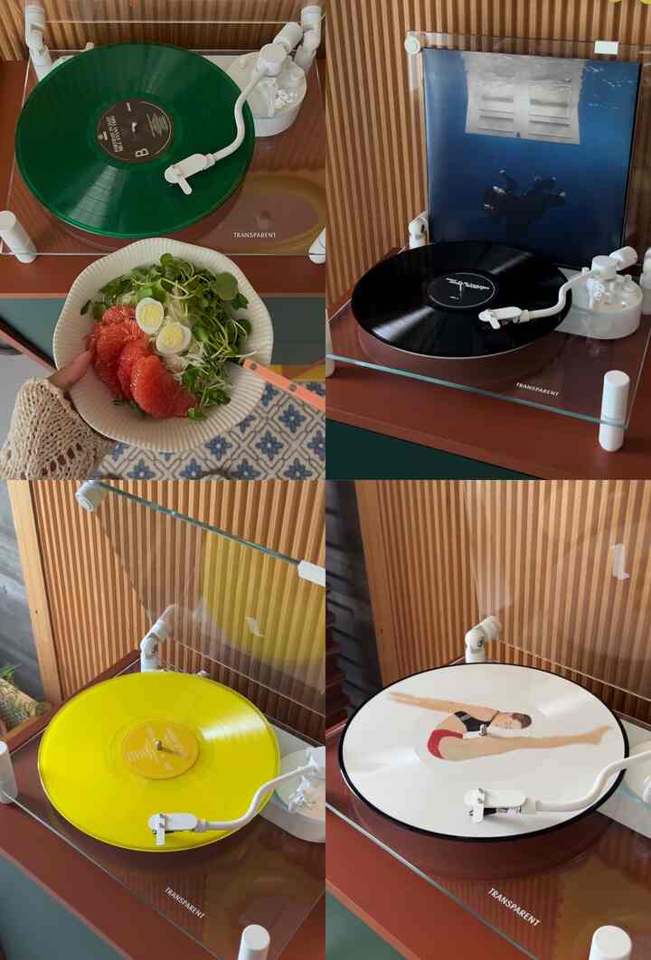 ブラウンの木目調の壁と透明カバーのターンテーブル4台、緑と黄色のLP盤が配置されたキッチン空間とサラダボウルが見える温かみのあるインテリア