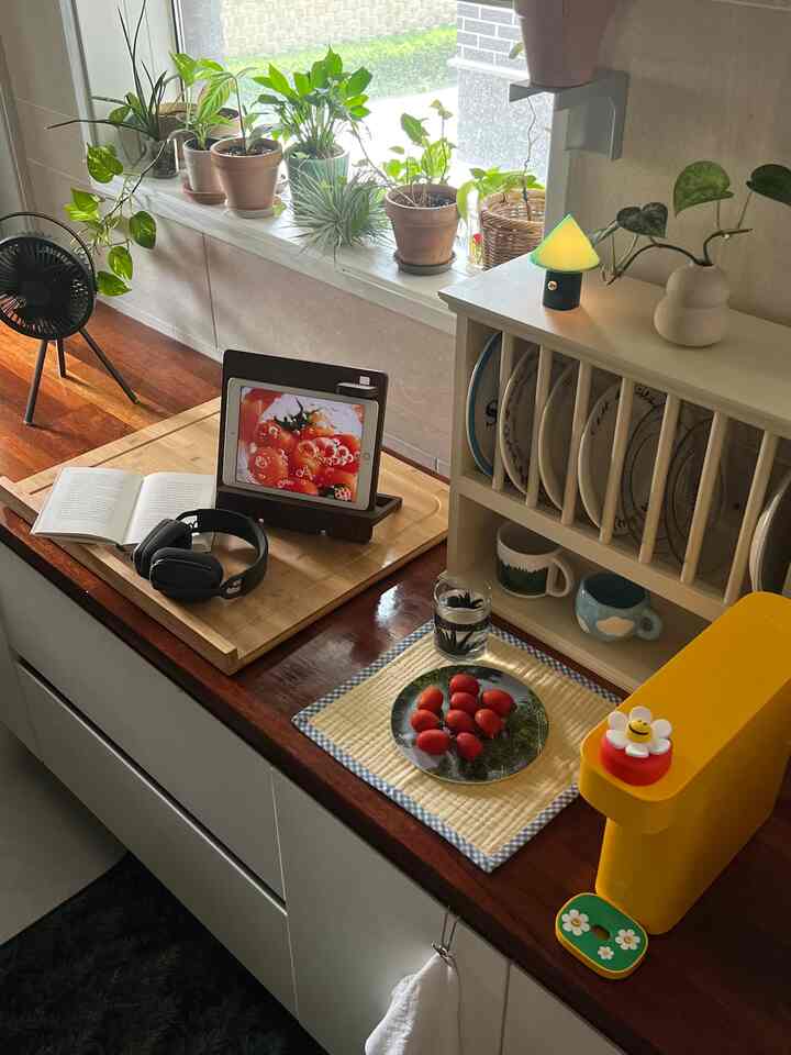 ウッドトーンとホワイトのキッチンスペース、窓際に置かれた植物とマグカップ、ムードランプが配置された雰囲気のあるおうちカフェ