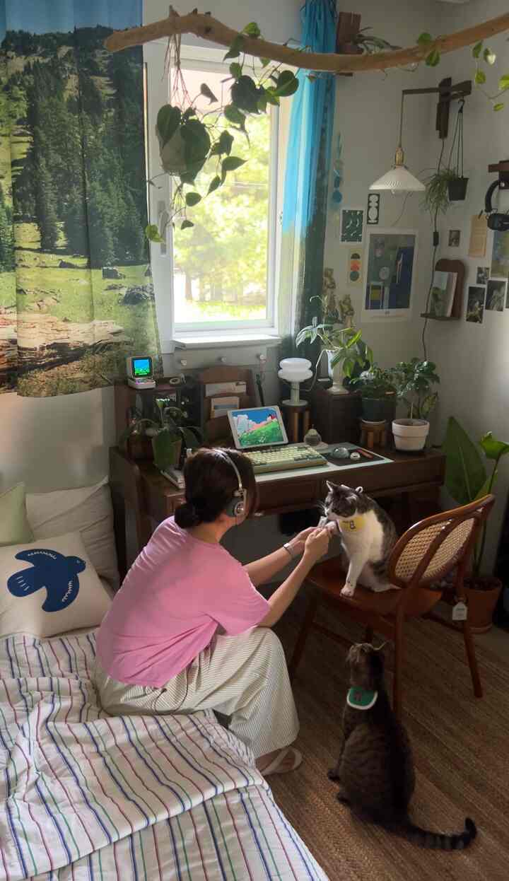 木目調と白を基調とした寝室兼ホームオフィス、ラタンチェアや多様な植物が配置された温かみのある空間