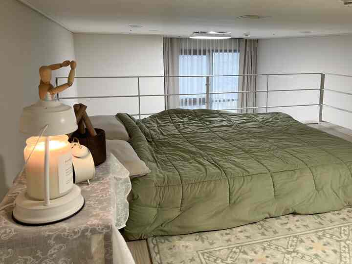 白い壁と緑の寝具が調和するロフトの寝室、低い天井の下にシンプルなベッドとナイトテーブルが配置された落ち着いた空間