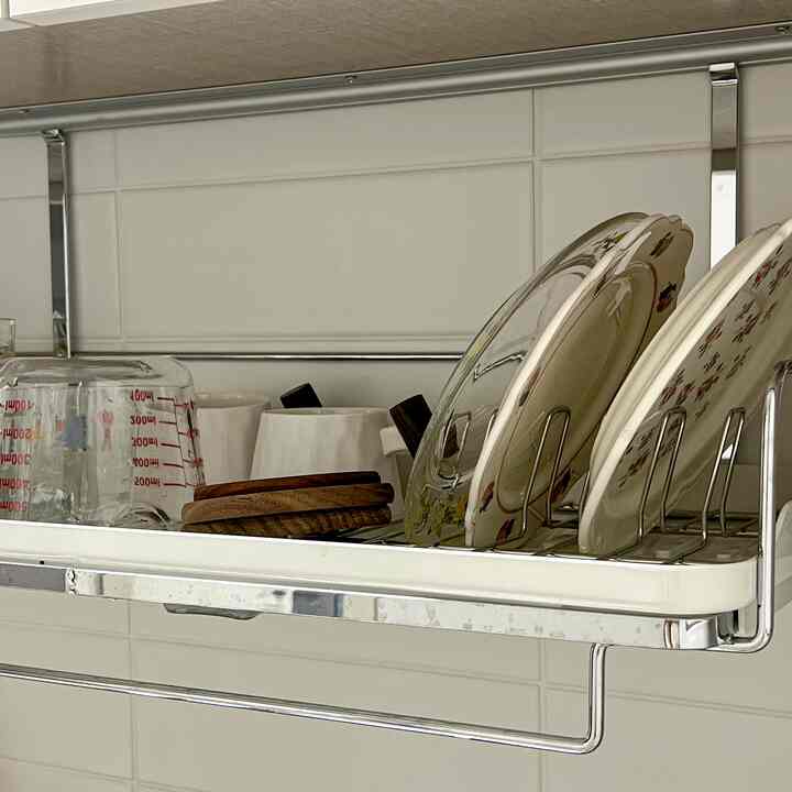 木目調とアイボリー色が調和するキッチンの天井取り付け食器乾燥ラックに、さまざまな皿と透明な計量カップが置かれた清潔感のある空間